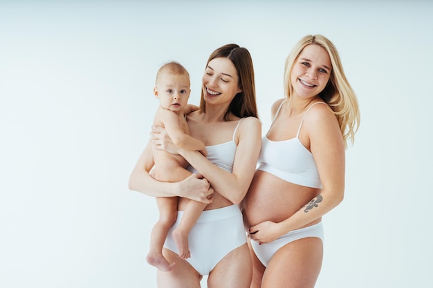 Mulher grávida feliz com barriga grande e linda mãe com bebê em fundo colorido - Mulheres jovens vestindo roupas íntimas esperando um bebê - Gravidez, maternidade, pessoas e conceito de expectativa