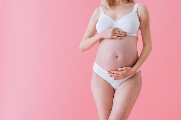 Mulher grávida feliz com barriga grande em fundo colorido - Jovem mulher vestindo cueca esperando um bebê - Gravidez, maternidade, pessoas e conceito de expectativa -