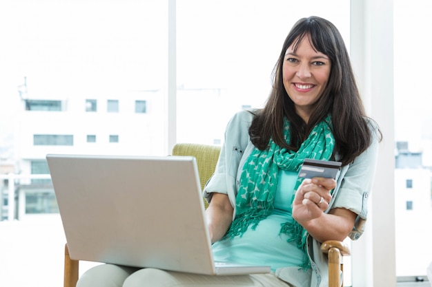 Mulher grávida feliz compras on-line em seu laptop em casa