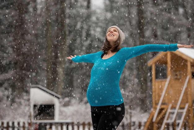 Mulher grávida feliz do lado de fora em um dia de neve com os braços bem abertos