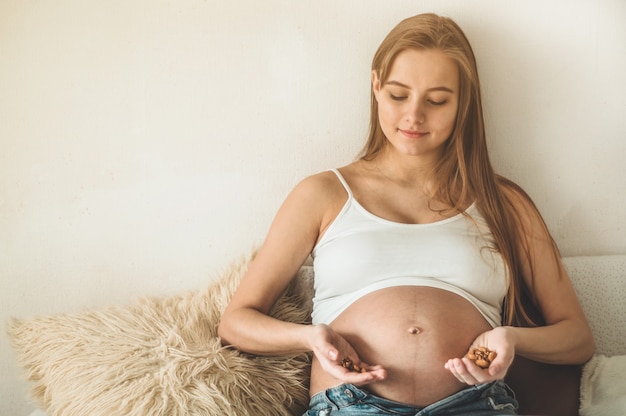 Mulher grávida feliz em casa comendo nozes frescas - amêndoas, nozes. Conceito de gravidez saudável.