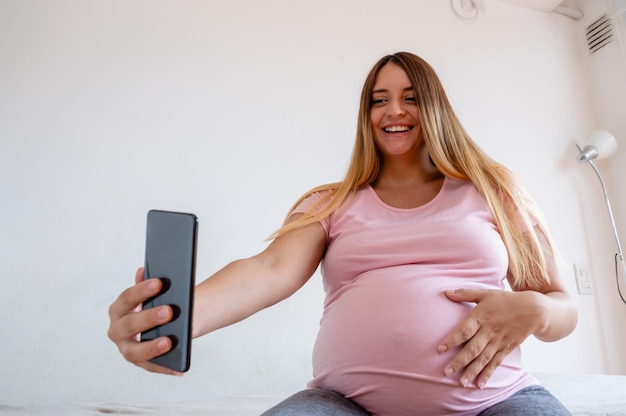 mulher grávida feliz em seu quarto sorrindo tira selfie com seu celular