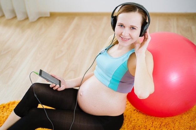 Mulher grávida feliz ouve música nos fones de ouvido e relaxa