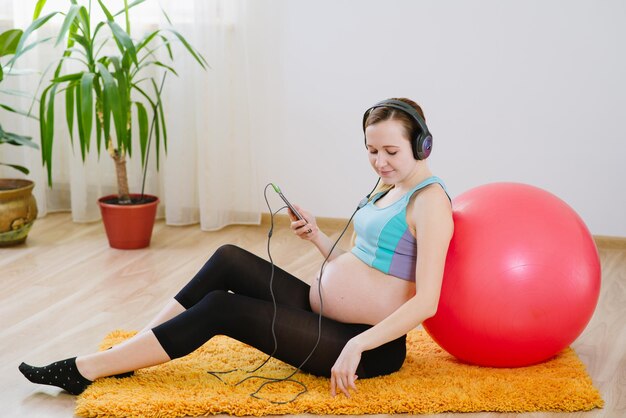 Mulher grávida feliz ouve música nos fones de ouvido e relaxa