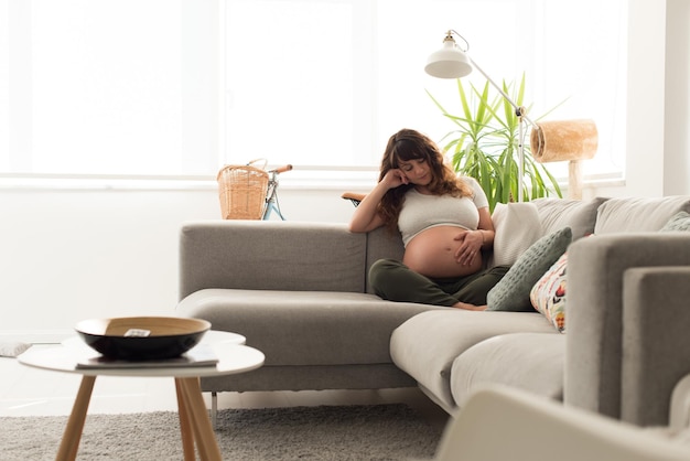 Mulher grávida feliz sentada e tocando sua barriga em casa