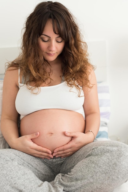 Mulher grávida feliz sentada e tocando sua barriga em casa