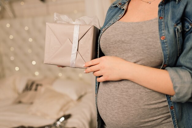 Mulher grávida feliz sentada em uma cama e tocando a barriga em casa sobre a árvore de natal