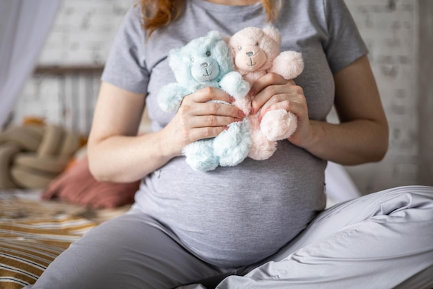 Mulher grávida feliz sentada na cama no quarto segurando dois ursinhos fofos esperando bebê gêmeos