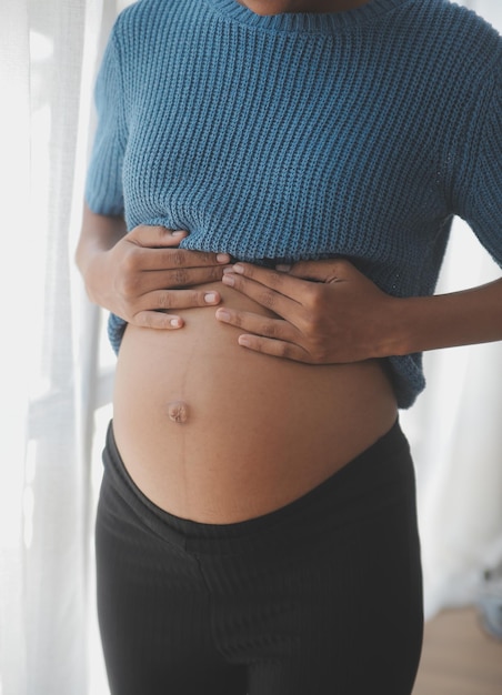 Mulher grávida feliz tocando a barriga na frente da parede branca