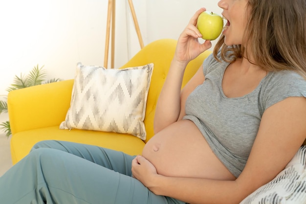 Mulher grávida irreconhecível a comer uma maçã saudável.