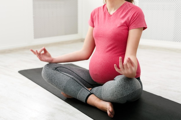 Mulher grávida irreconhecível meditando em casa, praticando ioga. Calma, relaxamento, conceito de gravidez saudável, espaço de cópia