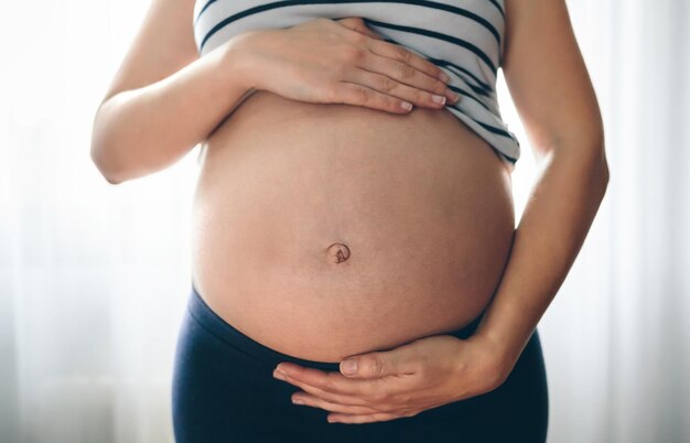 Mulher grávida irreconhecível segurando sua barriga no quarto