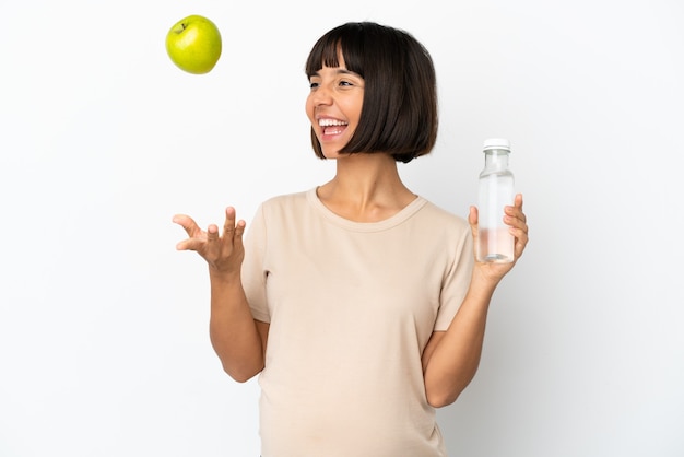 Mulher grávida jovem mestiça isolada no fundo branco com uma maçã e uma garrafa de água