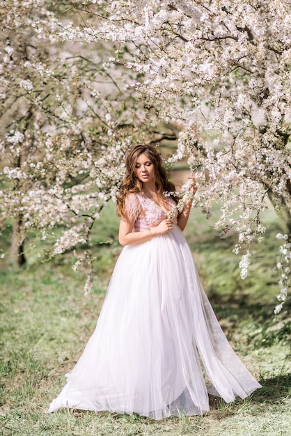 Mulher grávida linda em um vestido longo e leve caminha em um jardim primavera florescendo.