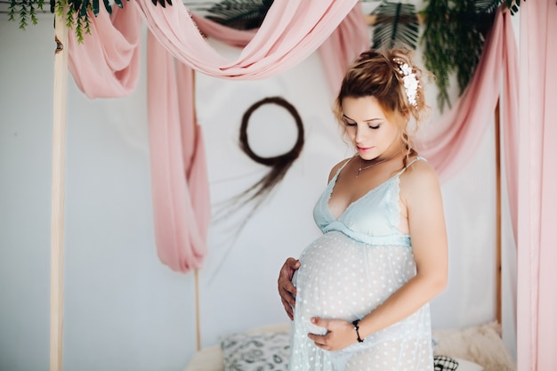 Mulher gravida loura que encontra-se em bedtouching pelas mãos no estômago.