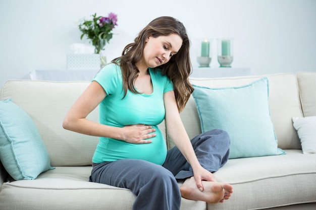 Mulher grávida massageando seus pés cansados no sofá