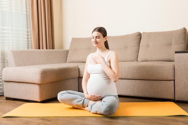 Mulher grávida meditando enquanto está sentada em posição de ioga Meditando na maternidade Conceito de ioga e fitness de gravidez na hora do coronavírus