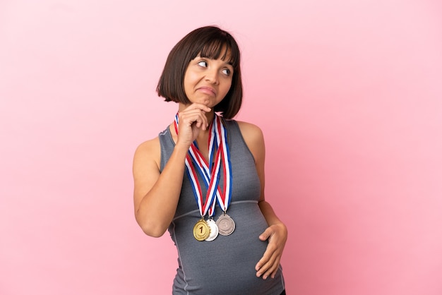 Foto mulher grávida mestiça com medalhas isoladas em um fundo rosa e olhando para cima