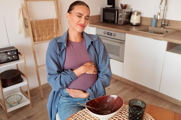 Mulher grávida na cozinha agarrando a barriga depois de comer demais