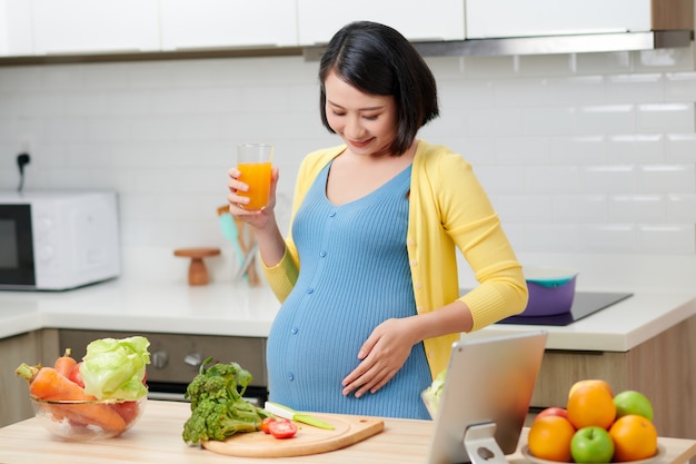 Mulher grávida na cozinha bebendo suco de fruta saudável