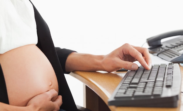 Mulher grávida no telefone trabalhando com um computador