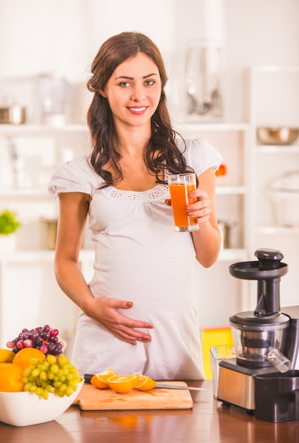 Mulher gravida no vestido branco que prepara o suco fresco.