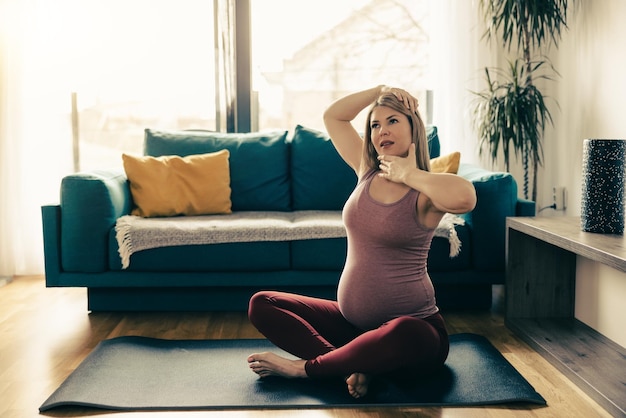 Mulher gravida nova que exercita em casa. Ela treino no colchonete e alongamento.