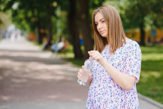 Mulher grávida parada no parque com uma garrafa de água