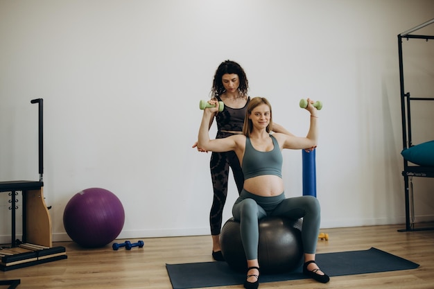 Mulher grávida pilates exercita treino no ginásio com personal trainer