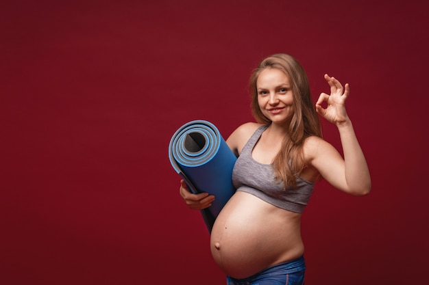 Mulher grávida positiva em roupas esportivas possui uma esteira de ginástica nas mãos dela.