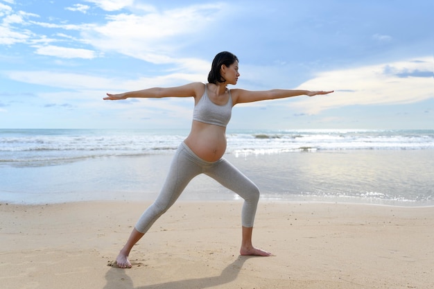 Foto mulher grávida pratica ioga e meditação enquanto faz pose de guerreiro dois fica na praia tranquila com cena da natureza conceito de estilo de vida saudável