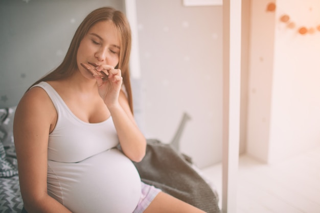 Mulher gravida que aprecia de comer o chocolate em casa.