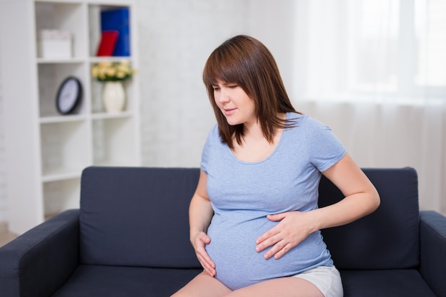 Mulher grávida recebendo uma contração em casa na sala de estar