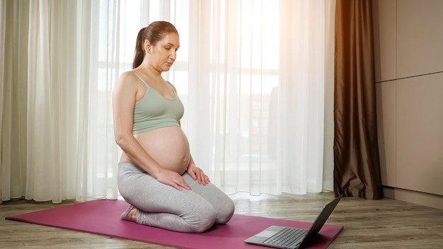 Mulher grávida se aquece assistindo tutorial via laptop no tapete