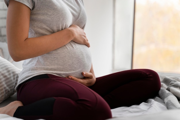 Mulher grávida segurando a barriga enquanto está sentada na cama