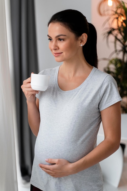 Foto mulher grávida segurando a barriga enquanto toma uma xícara de chá