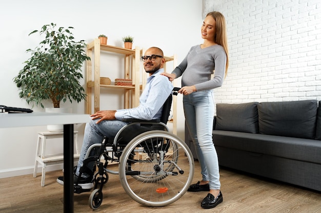Mulher grávida segurando a mão do marido deficiente sentado em uma cadeira de rodas