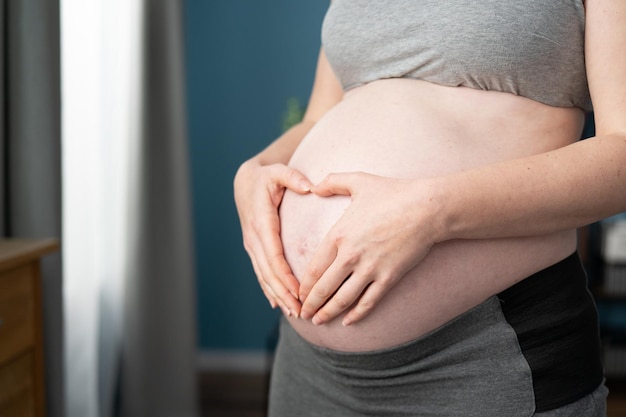 Mulher grávida segurando as mãos em forma de coração em sua barriga de grávida com dedos de coração