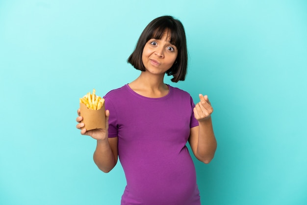 Mulher grávida segurando batatas fritas sobre fundo isolado fazendo gesto de dinheiro