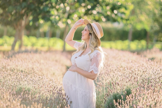 Mulher grávida segurando chapéu e mão na barriga no campo de lavanda