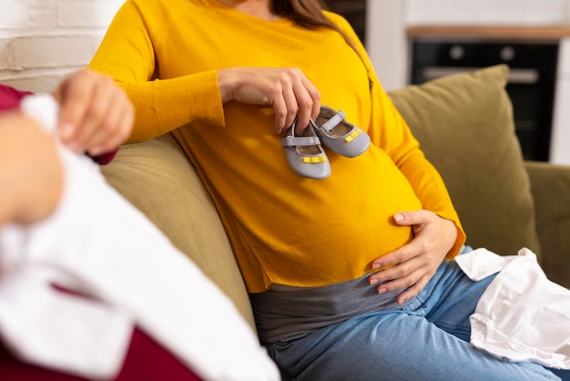 Mulher grávida segurando macacão branco de bebê se preparando para o parto durante a gravidez