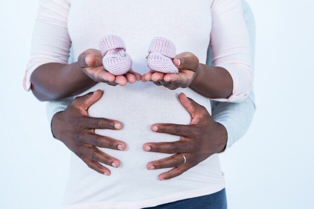 Mulher grávida segurando sapatos de bebê enquanto o marido toca sua barriga