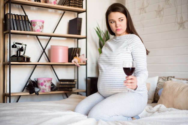 Mulher grávida segurando um copo de vinho. Futura mãe bebendo álcool enquanto esperava um bebê. Conceito de estilo de vida pouco saudável e nocividade.