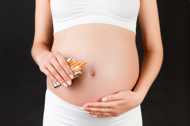 Mulher grávida segurando um maço de cigarros