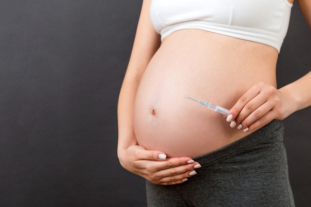 mulher grávida segurando uma seringa contra a barriga