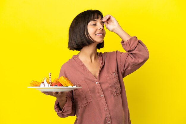 Mulher grávida segurando waffles isolados em um fundo amarelo e sorrindo muito