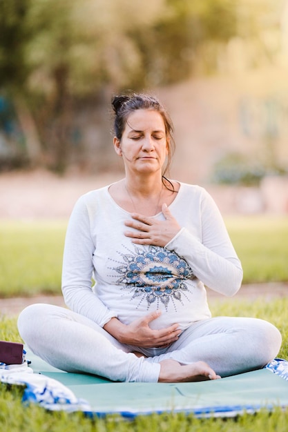 Mulher grávida sentada em pose de meditação em um parque ao ar livre