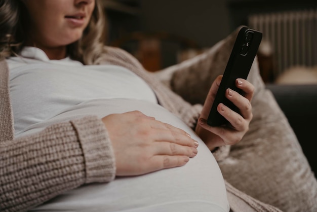 Mulher grávida sentada em seu sofá usando seu celular