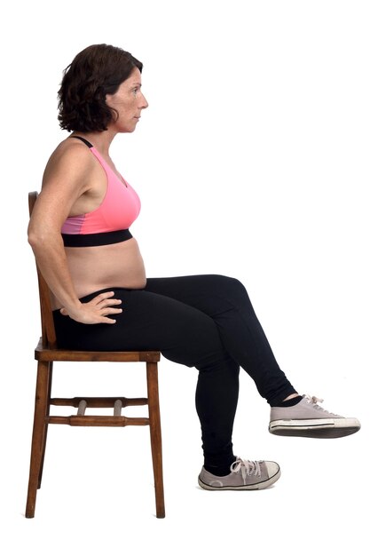 Mulher grávida sentada em uma cadeira no fundo branco, com as mãos no quadril