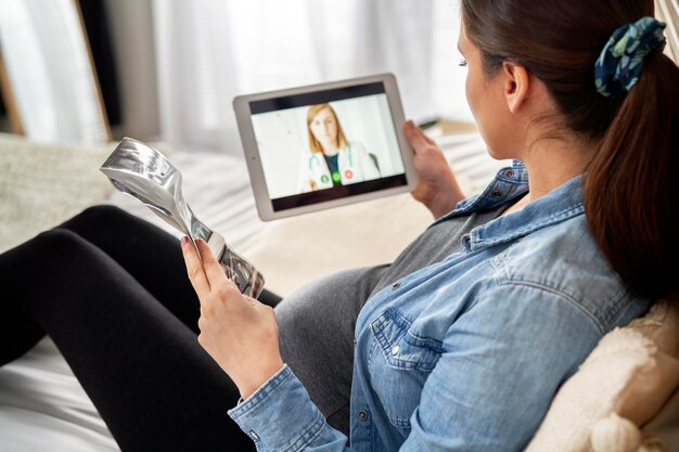 Foto mulher grávida sentada na cama e tendo uma consulta on-line com um obstetra